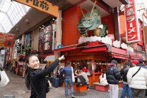 Karina Fu terpesona oleh tanda naga yang unik di Dotonbori, jalan kuliner terkenal di Osaka, yang menawarkan pesta tidak hanya untuk selera tetapi juga mata. Area ini terkenal dengan tampilan iklan dinamis di atas restoran, mulai dari figur kepiting kolosal hingga lampu neon bercahaya.