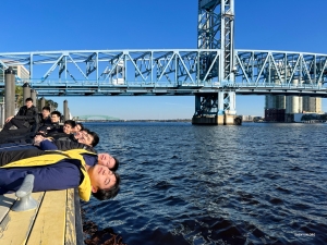 Beristirahat di tepi perairan, anggota Perusahaan Internasional Shen Yun menikmati pemandangan di bawah Jembatan Jalan Utama yang geometris di Jacksonville, Florida.